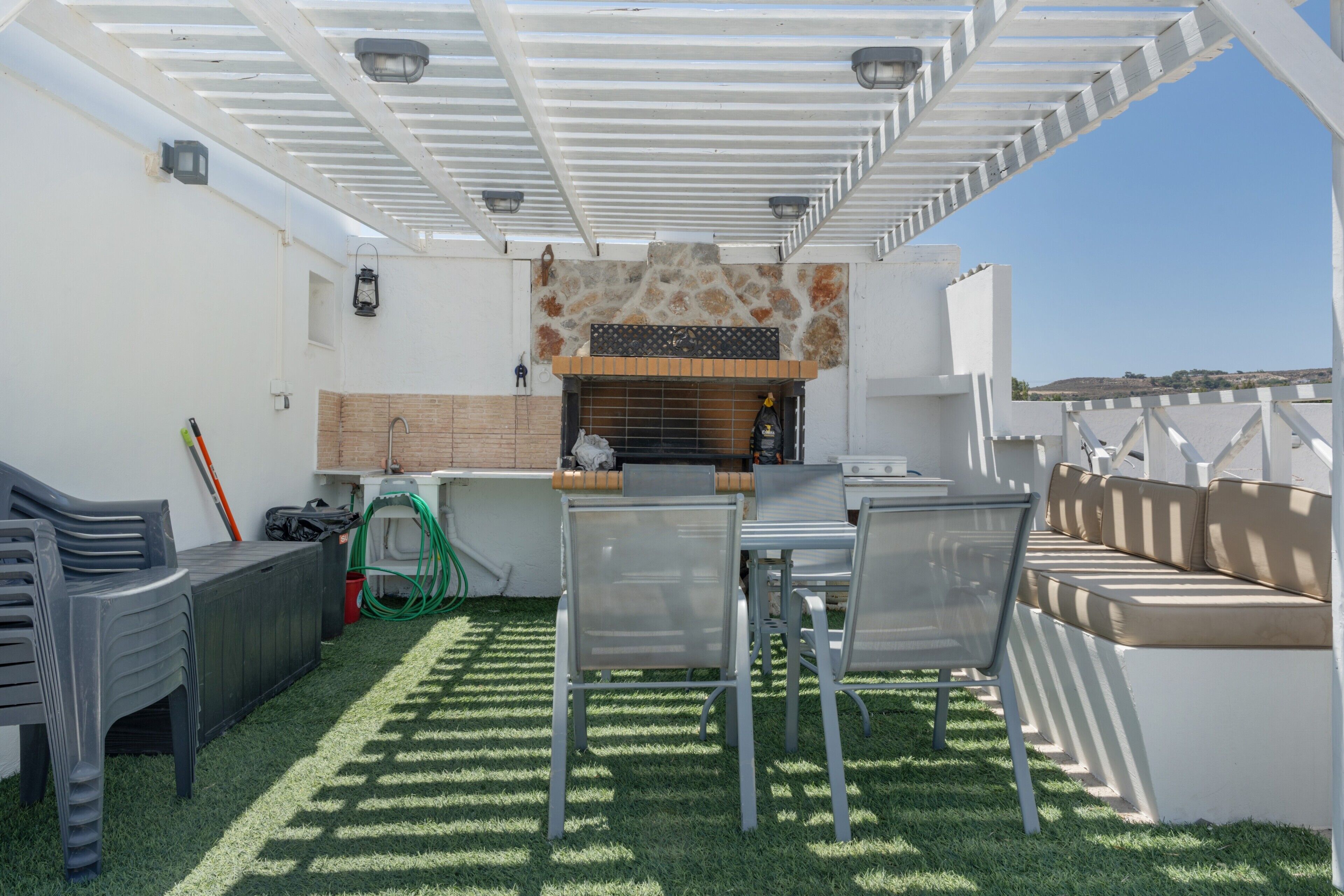 An outdoor patio with a grill, seating, and a pergola structure.