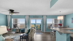 A spacious living room with a view of the ocean, a ceiling fan, and a dining area with a kitchen counter. - 🌊Gulf View-Steps to Beach-Heated Pool-Islander Beach Resort 2002🌅 (Fort Walton Beach)