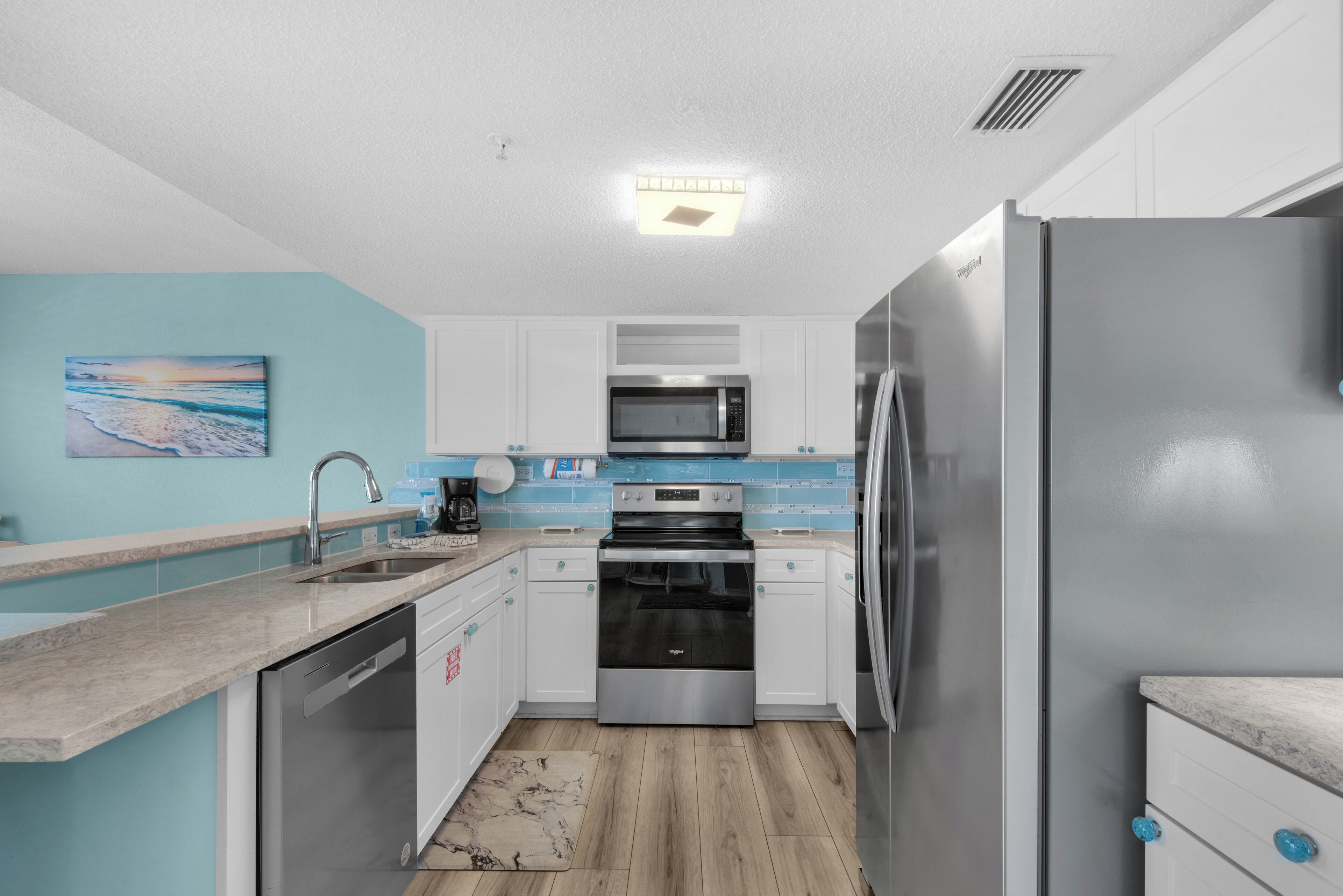 A modern kitchen with white cabinets, a stainless steel refrigerator, a microwave, and a dishwasher.