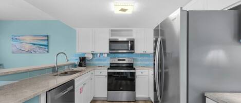 A modern kitchen with white cabinets, a stainless steel refrigerator, a microwave, and a dishwasher.