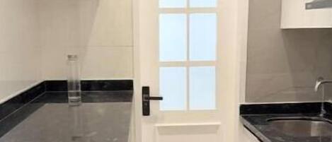 A narrow kitchen with white cabinets, a black countertop, and a white door with a window.