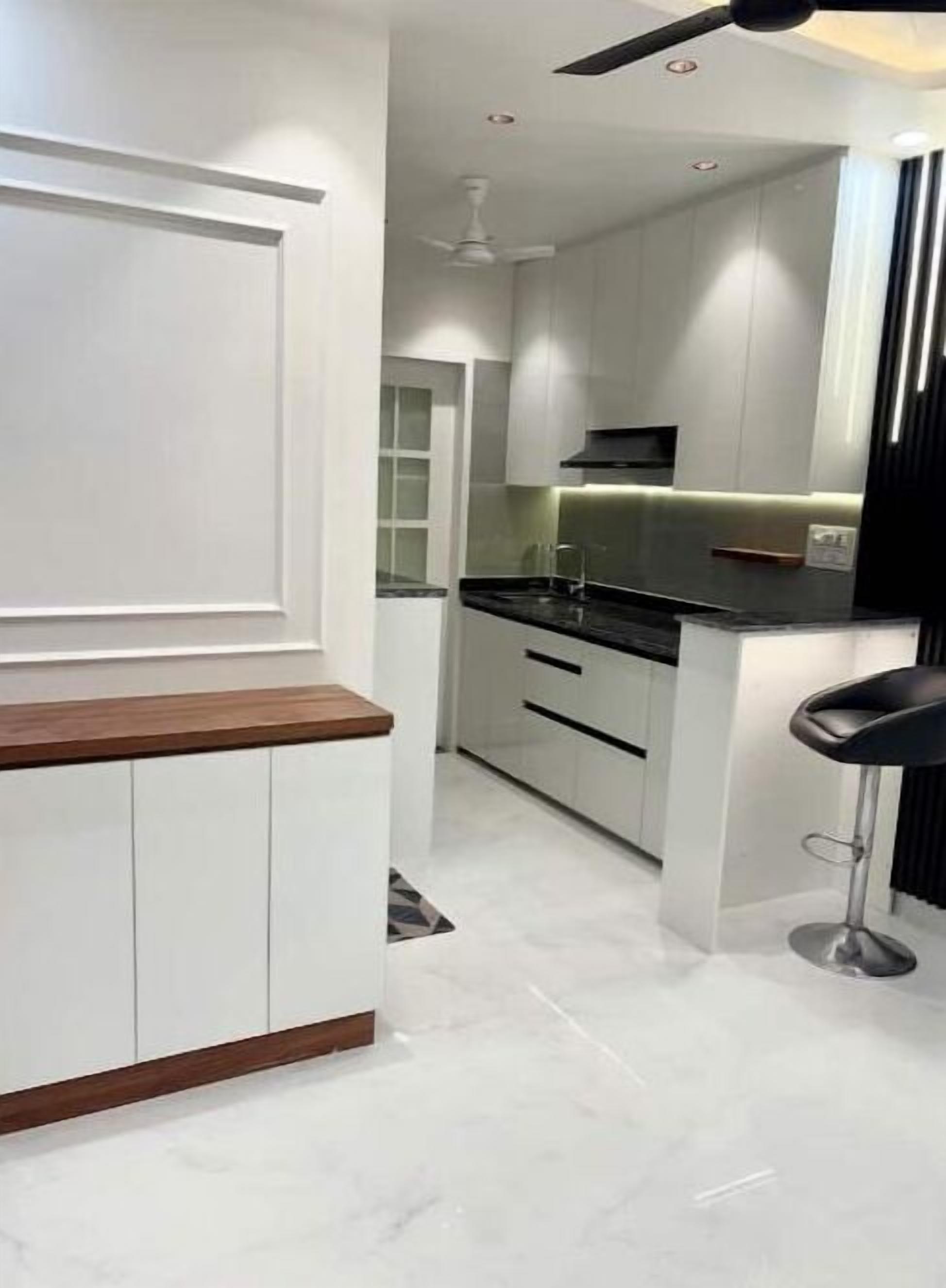 Cocina moderna con armarios blancos, encimera negra y un taburete de bar.