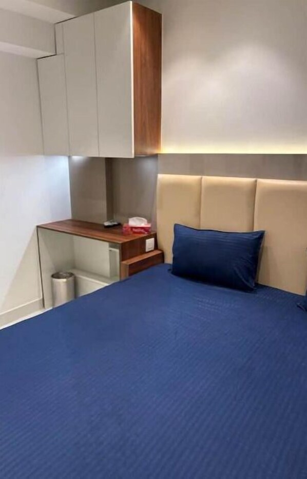 A compact hotel room with a bed, a small desk, and a built-in wardrobe. - Royal Apartment in Dlf Capital Greens West Delhi (Delhi)