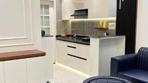 A modern kitchen with white cabinetry, a black countertop, and a built-in stove. There is a blue upholstered sofa and ottoman in the living area.