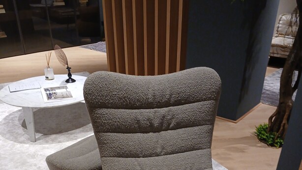 Un fauteuil moderne, doté d’un tissu texturé et d’un design original à plusieurs niveaux, est placé sur un plancher de couleur claire, agrémenté d’un tapis blanc.