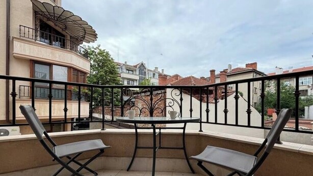 A balcony with two chairs and a table, overlooking a residential area with houses and a clear sky. - MarkApart 3: Apartment in Downtown Ruse (Ruse)