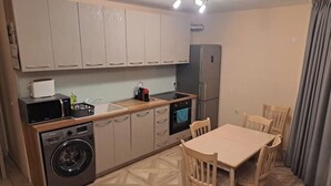 A compact kitchen with a washing machine, microwave, and a small dining area with chairs and a table. - MarkApart 3: Apartment in Downtown Ruse (Ruse)