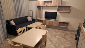 A compact living space with a sofa, a dining table, and a TV mounted on a wall. - MarkApart 3: Apartment in Downtown Ruse (Ruse)