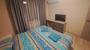 A hotel room with a bed, a TV on a wooden cabinet, and a window with curtains. - MarkApart 3: Apartment in Downtown Ruse (Ruse)