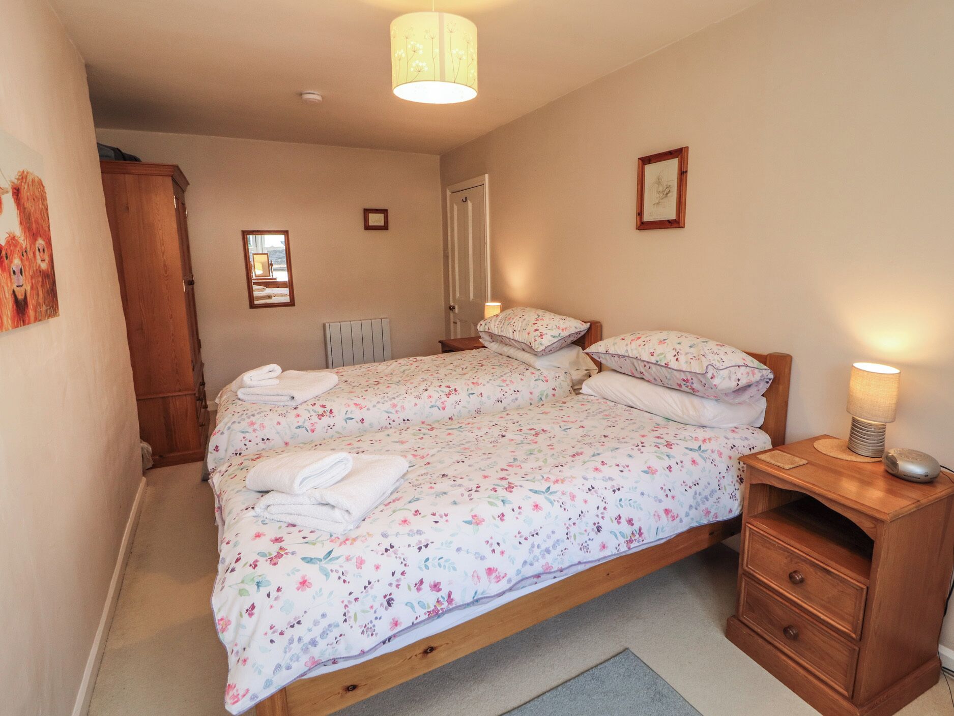 A bedroom with two single beds, a wooden nightstand, a bedside lamp, a radiator, and a door.
