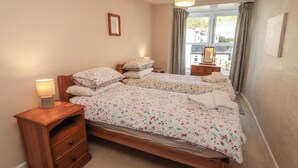 Quarto com duas camas, uma mesinha de cabeceira com abajur, cômoda e janela com cortinas.