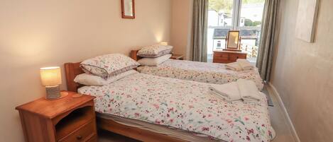 A bedroom with two beds, a bedside table with a lamp, a dresser, and a window with curtains.