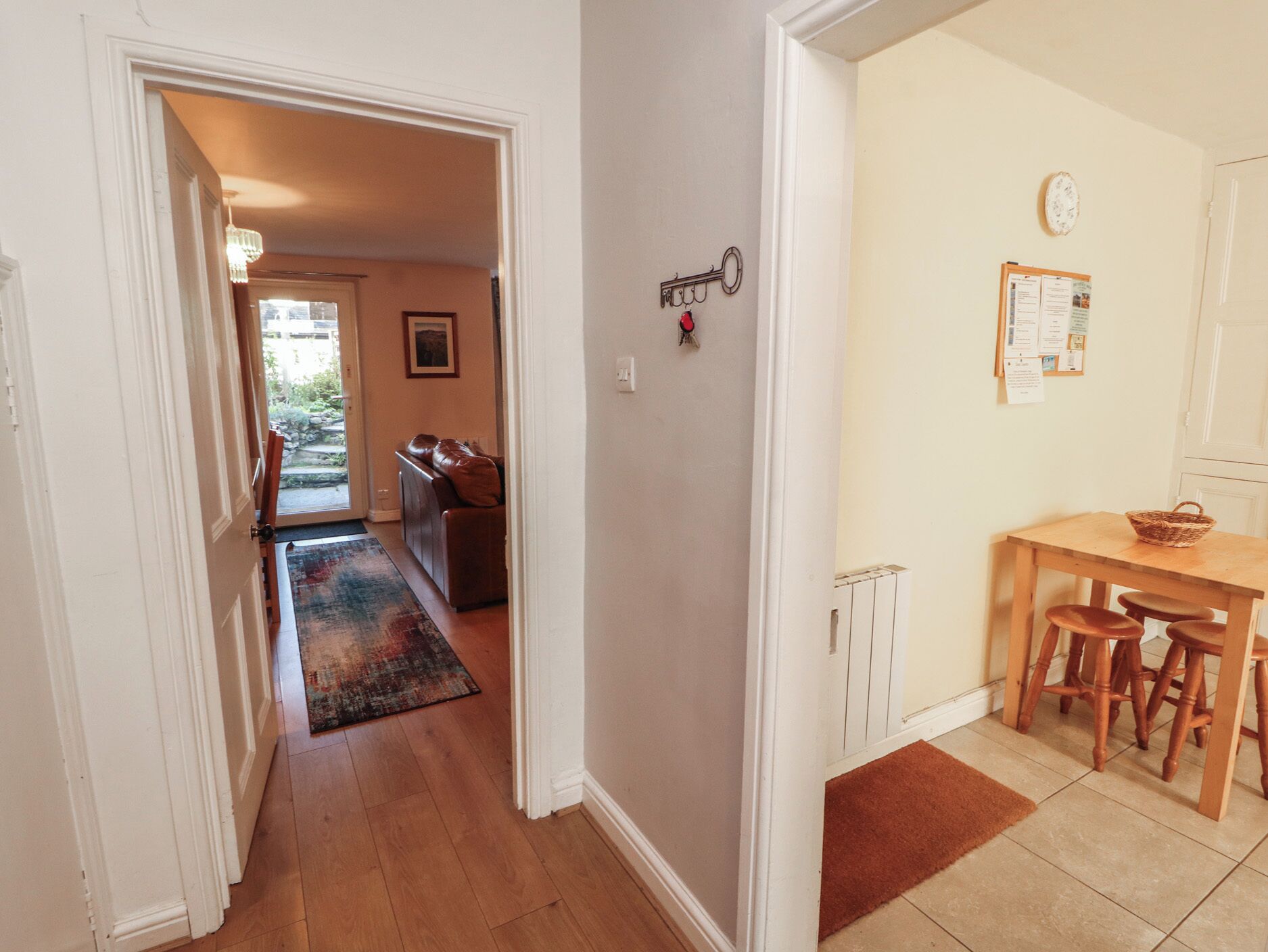 A hallway leading to a living room with a brown leather sofa, a dining area with a wooden table and chairs, and a kitchen with a radiator.