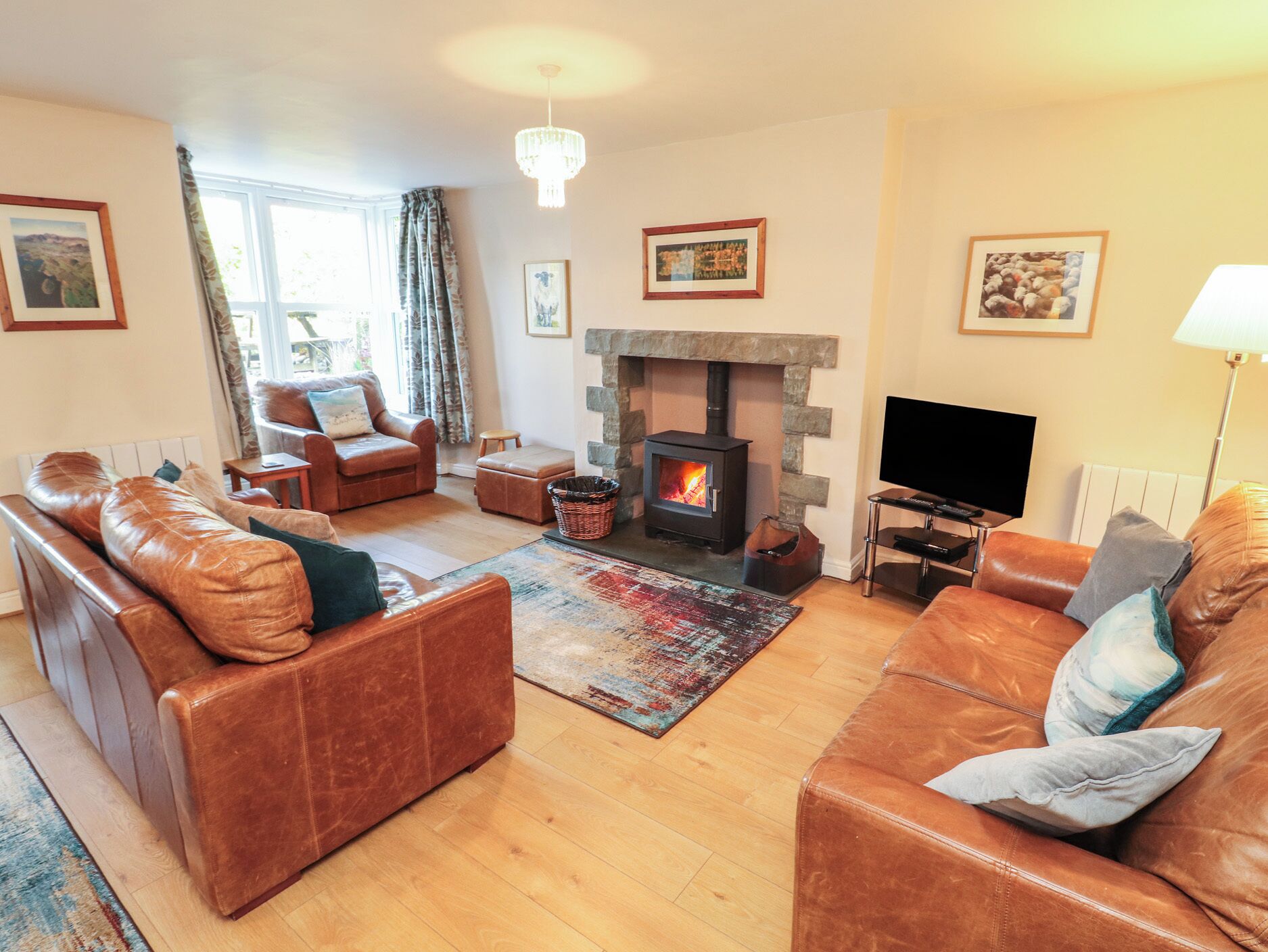 A living room with leather sofas, a stone fireplace, a television, and framed pictures on the walls.