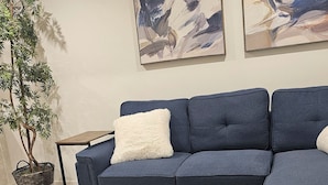 A living room with a sectional sofa, a wooden coffee table, a potted plant, and abstract paintings on the wall.