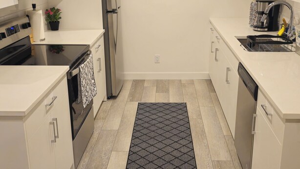 A modern kitchen with white cabinetry, stainless steel appliances, and a black and white patterned rug.