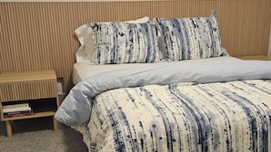 A bedroom with a bed, a wooden nightstand with books, and two abstract paintings on the wall.