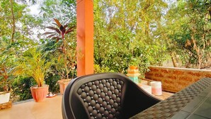 Un espacio de estar al aire libre cubierto con una mesa y sillas, rodeado de plantas en macetas y árboles.