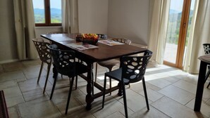 A dining area with a wooden table, six chairs, a fruit bowl, and a view through large windows. - Villa for family/friends, few minutes from the most beautiful medieval villages (Umbria)