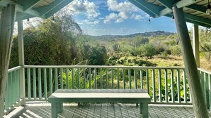 Un espacio al aire libre cubierto con un banco, barandillas de madera y vistas a un paisaje verde.