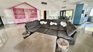 Un salón amplio con un sofá modular grande, un mueble rosa y una cocina moderna al fondo.