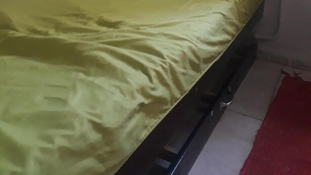 A small, single-bed room with a green bedspread, a metal frame, and a red rug on the floor. - Hostel Sapucali (Rio de Janeiro)