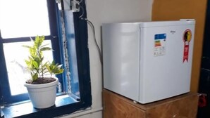 A small room with a window, a potted plant, a white refrigerator, and a wooden cabinet. - Hostel Sapucali (Rio de Janeiro)
