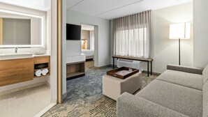A modern hotel room with a large mirror, a wooden vanity, a sofa, and a flat-screen TV. - Springhill Suites Pittsburgh Airport (Coraopolis)