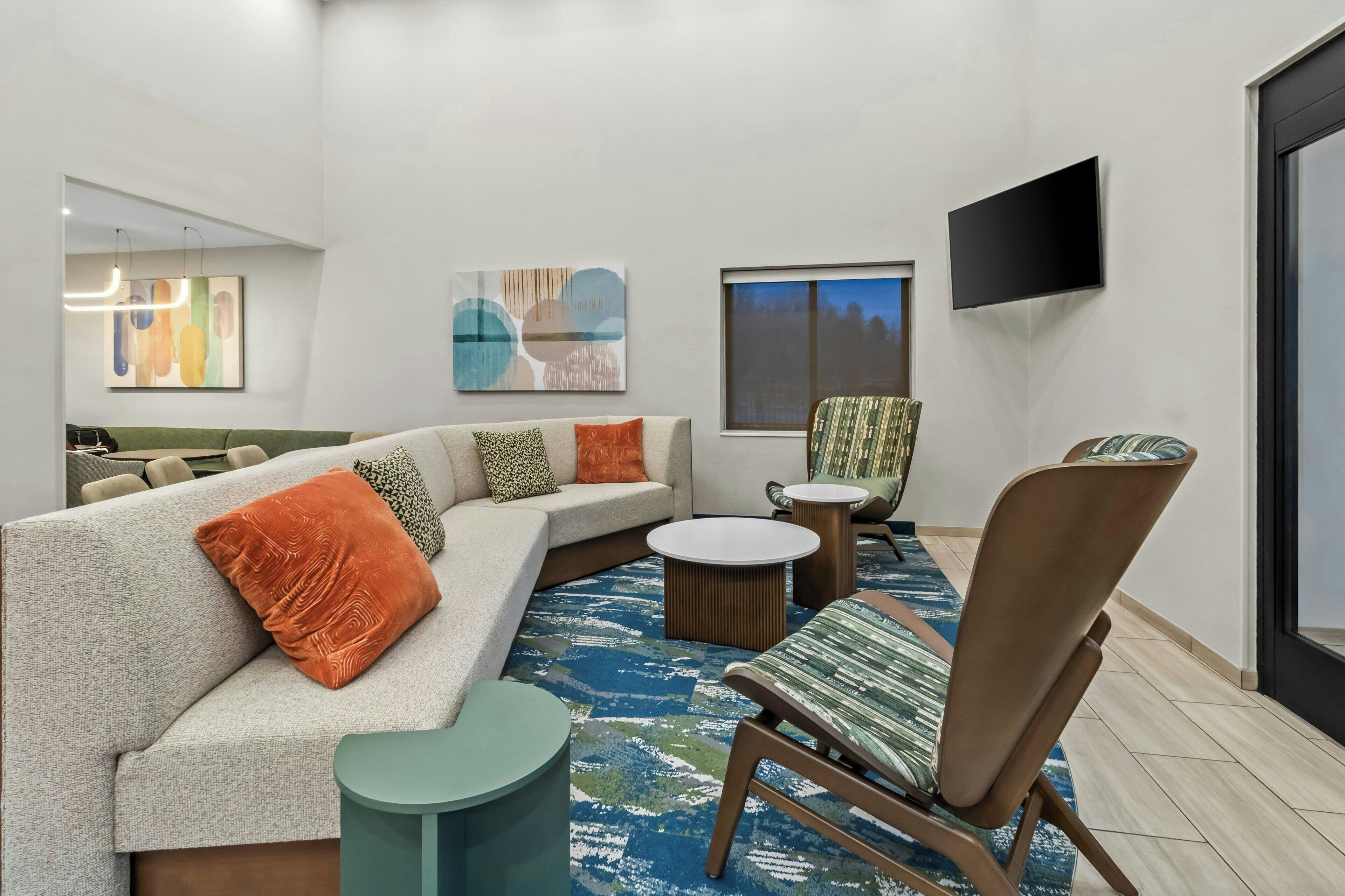 A modern living room with a sectional sofa, a patterned armchair, a round coffee table, and a flat-screen TV mounted on the wall.