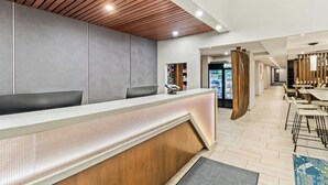 A modern reception area with a wooden ceiling, a reception desk, and a seating area with tables and chairs. - Springhill Suites Pittsburgh Airport (Coraopolis)