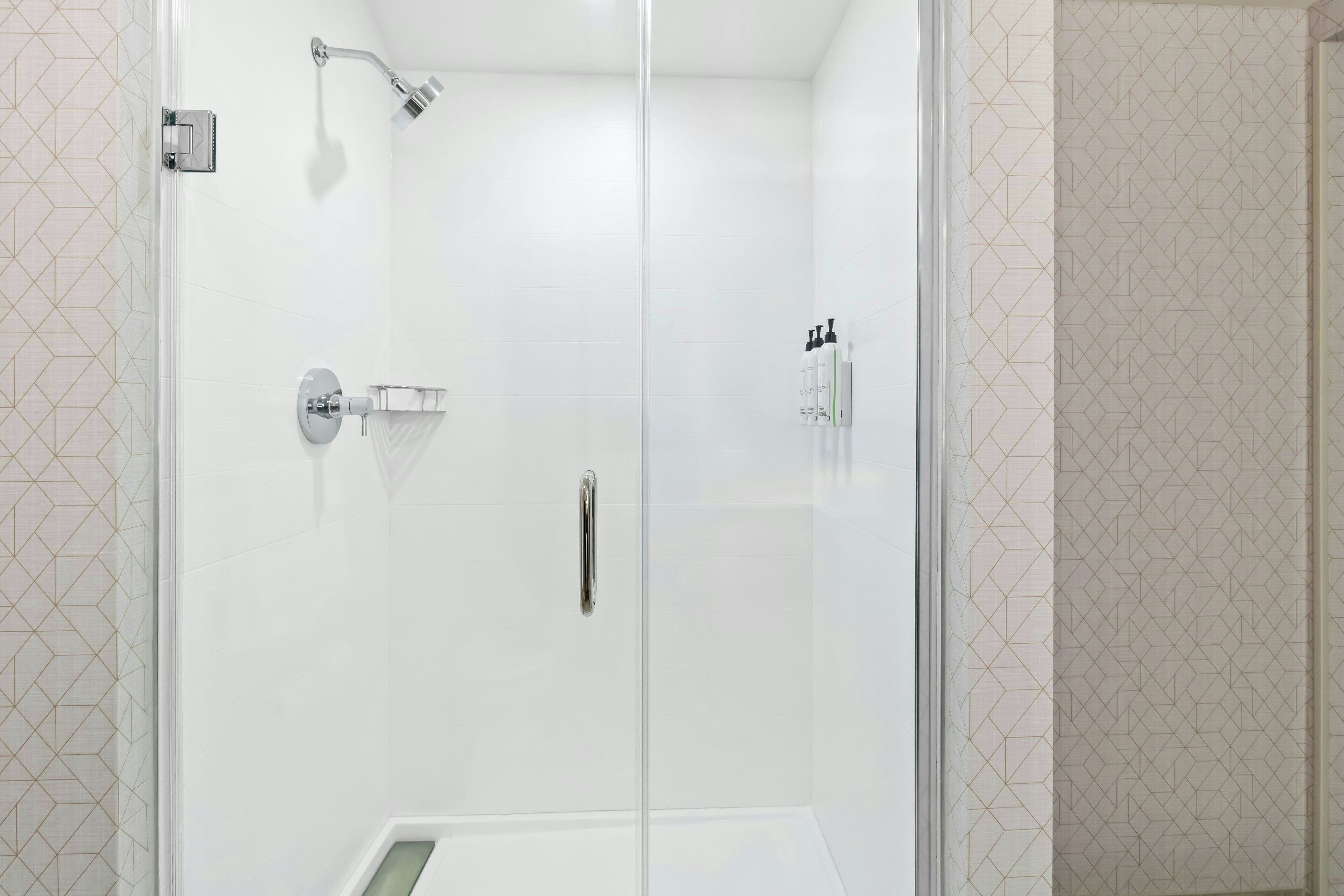 A modern bathroom with a glass shower enclosure, a handheld showerhead, and a wall-mounted towel rack.