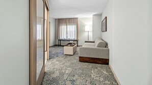 A hotel room with a sofa, a small table, a lamp, and a view of the outdoors through a window with curtains. - Springhill Suites Pittsburgh Airport (Coraopolis)