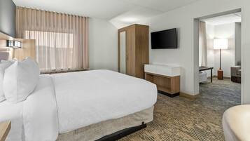 Une chambre d’hôtel avec un lit, un bureau, une télévision et une salle de bain visible à travers une porte ouverte.