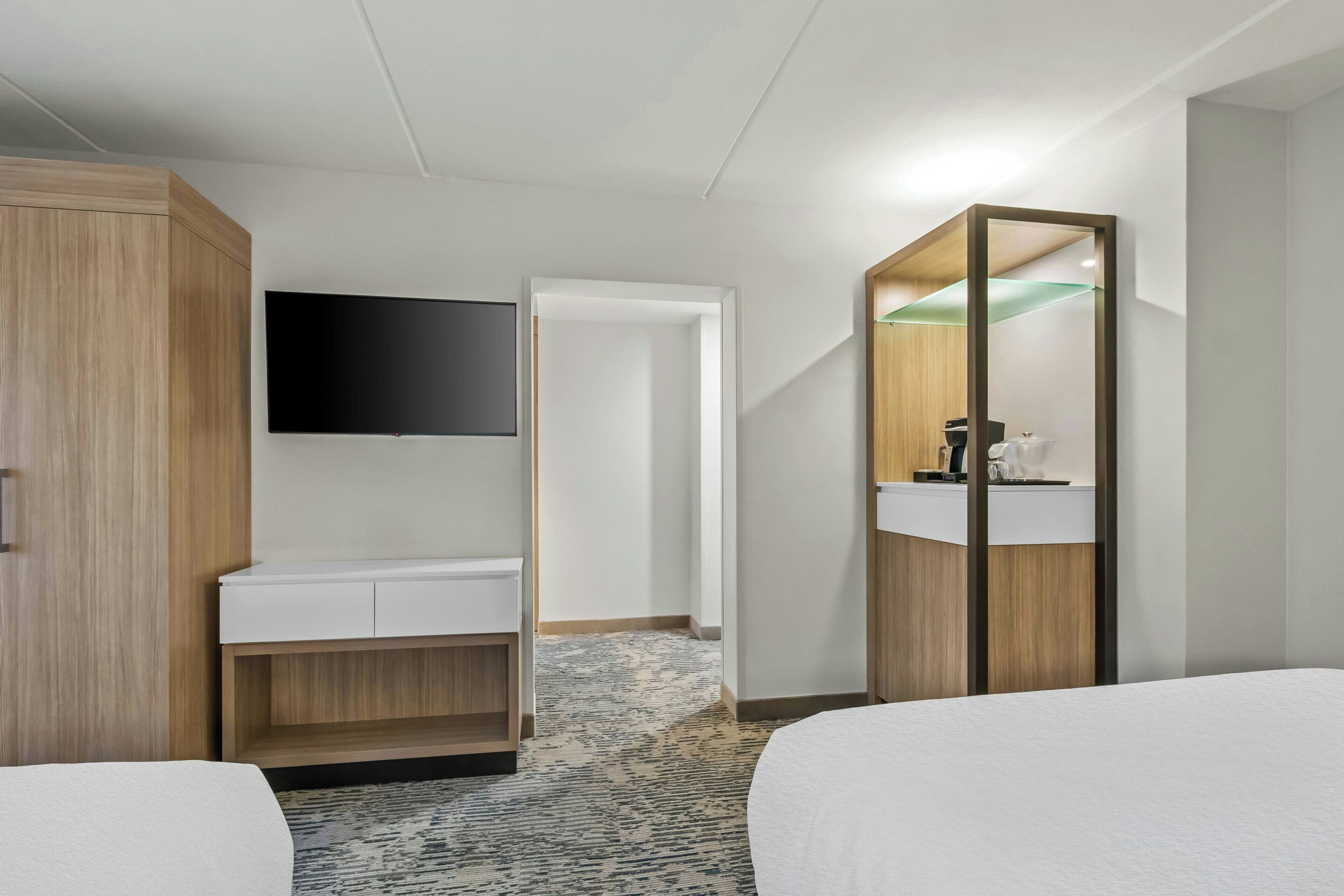A hotel room with a bed, a desk, a mirror, and a TV.