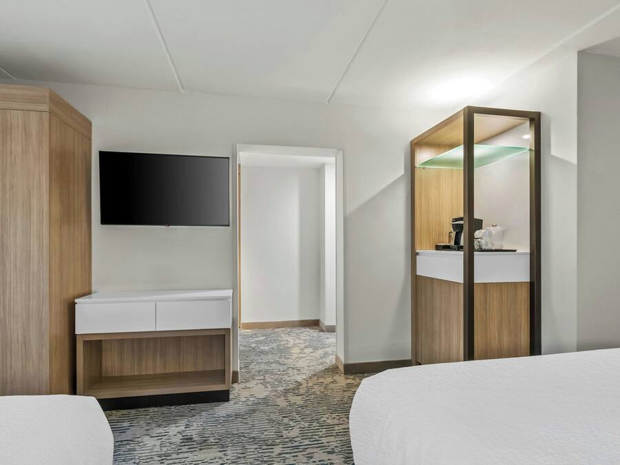 A hotel room with a bed, a desk, a mirror, and a TV.