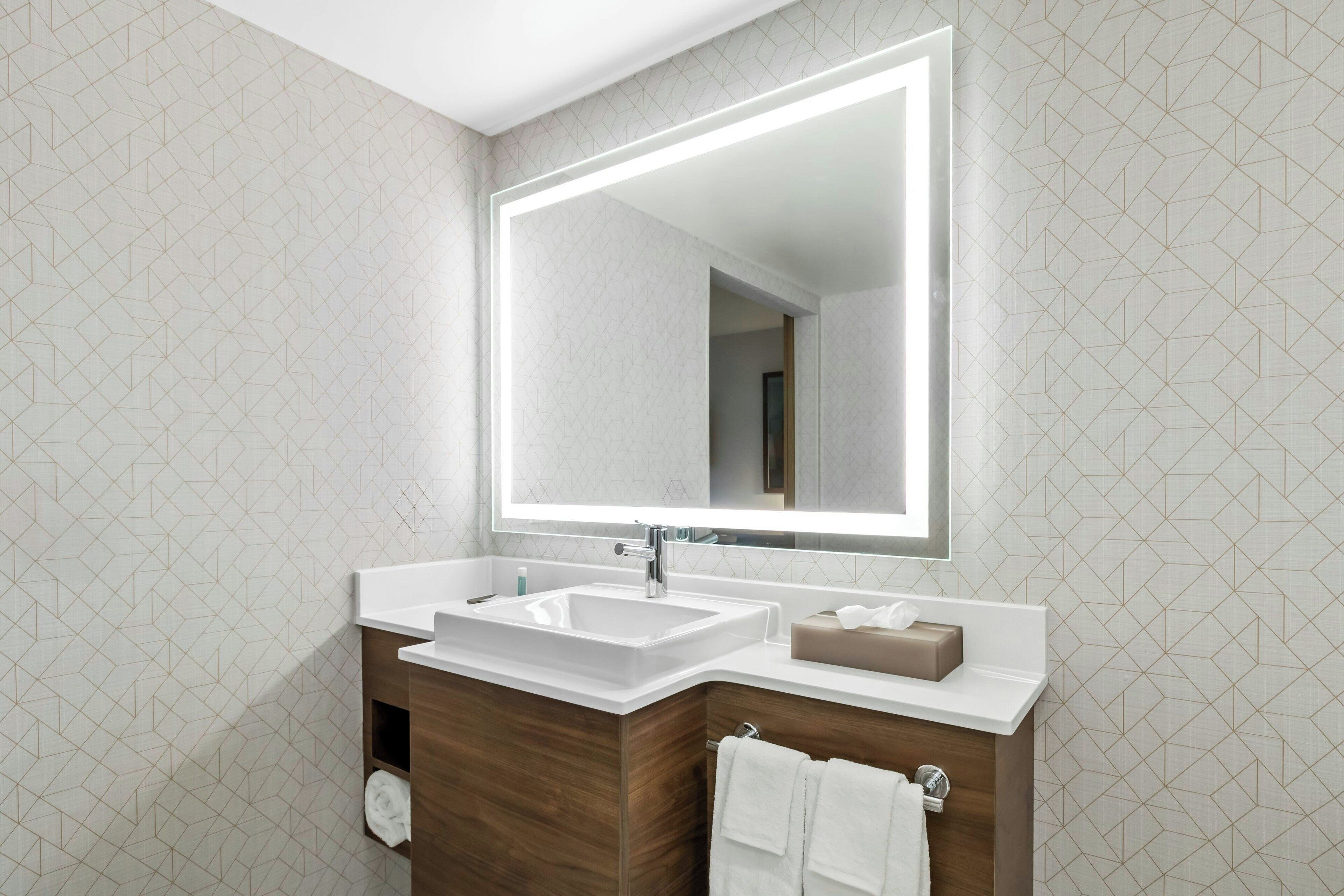 A modern bathroom with a large mirror, two sinks, and a wooden vanity.
