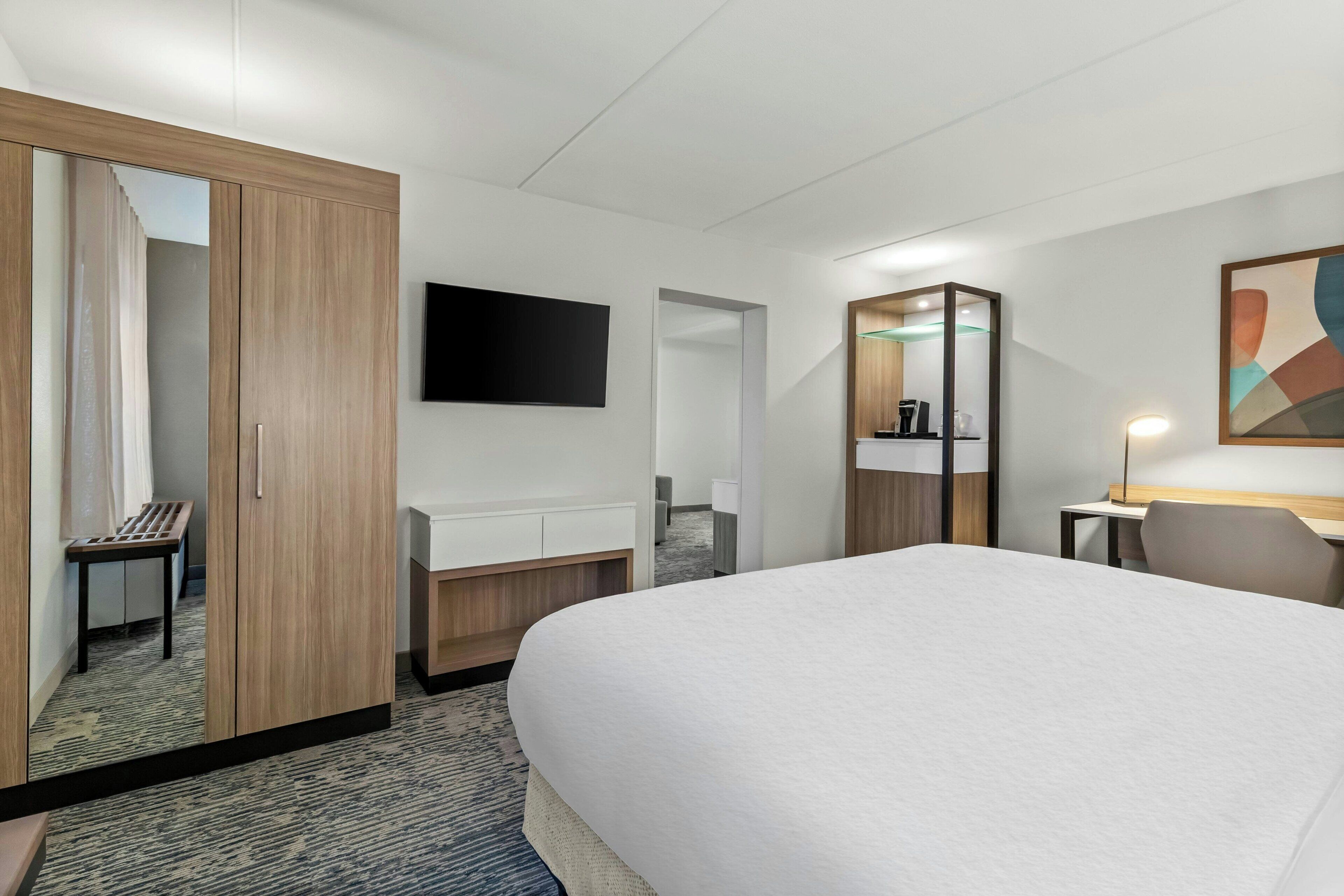 A hotel room with a large bed, a desk, a chair, a TV, and a wardrobe.