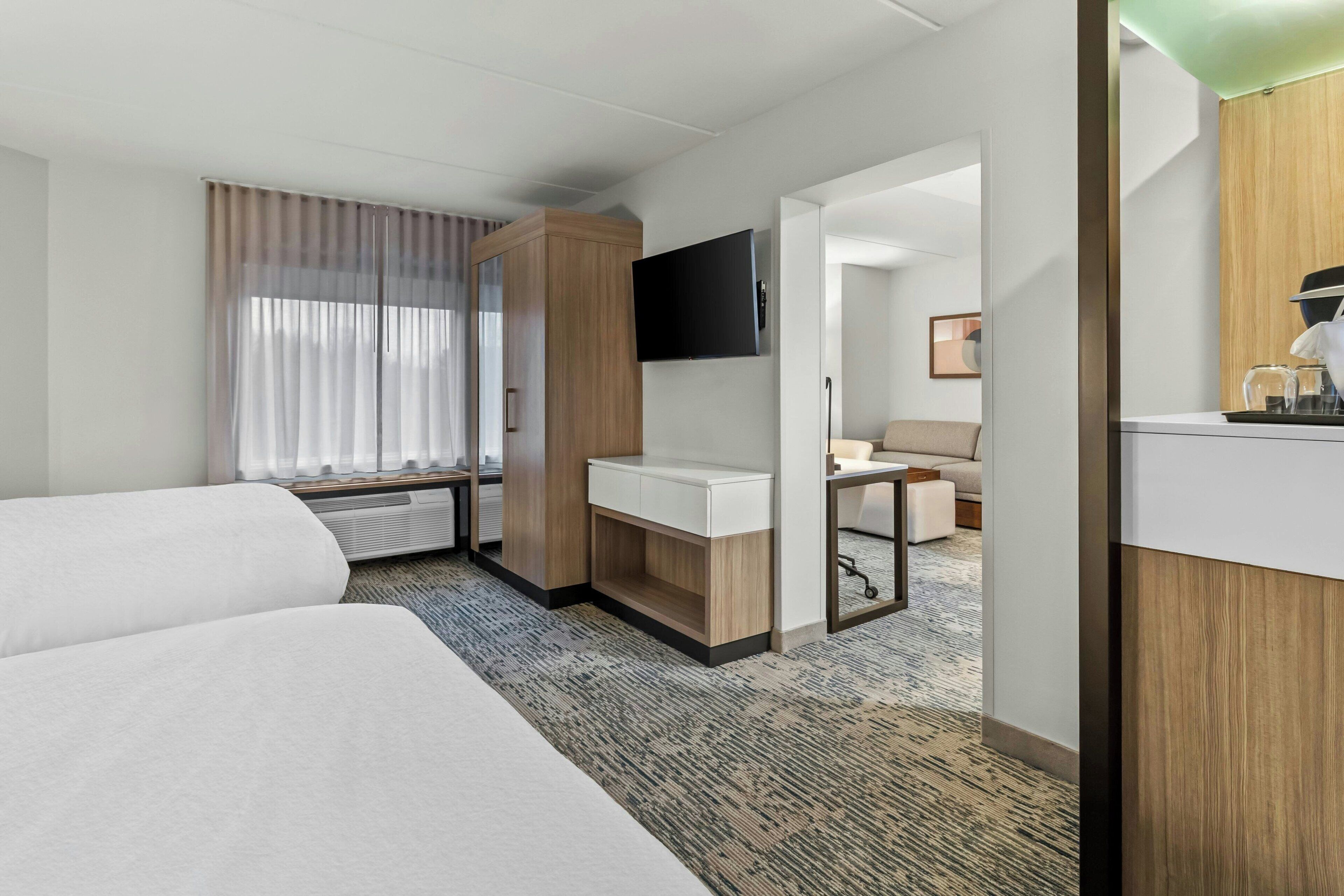 Une chambre d’hôtel avec deux lits, un bureau doté d’un téléviseur à écran plat, un minibar et une vue sur le couloir.