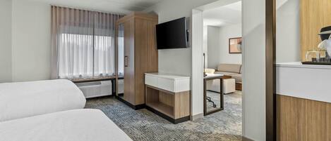 Une chambre d’hôtel avec deux lits, un bureau doté d’un téléviseur à écran plat, un minibar et une vue sur le couloir.