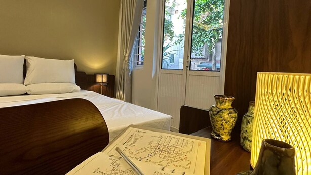 Een hotelkamer met een bed, een bureau met een notitieboekje, een lamp en decoratieve vazen.