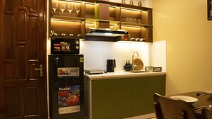 A compact kitchen with a refrigerator, a microwave, and a sink. There are wine glasses on a shelf above the stove.