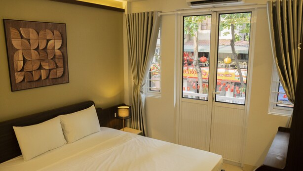 A hotel room with a bed, a nightstand, a lamp, and a window with curtains.
