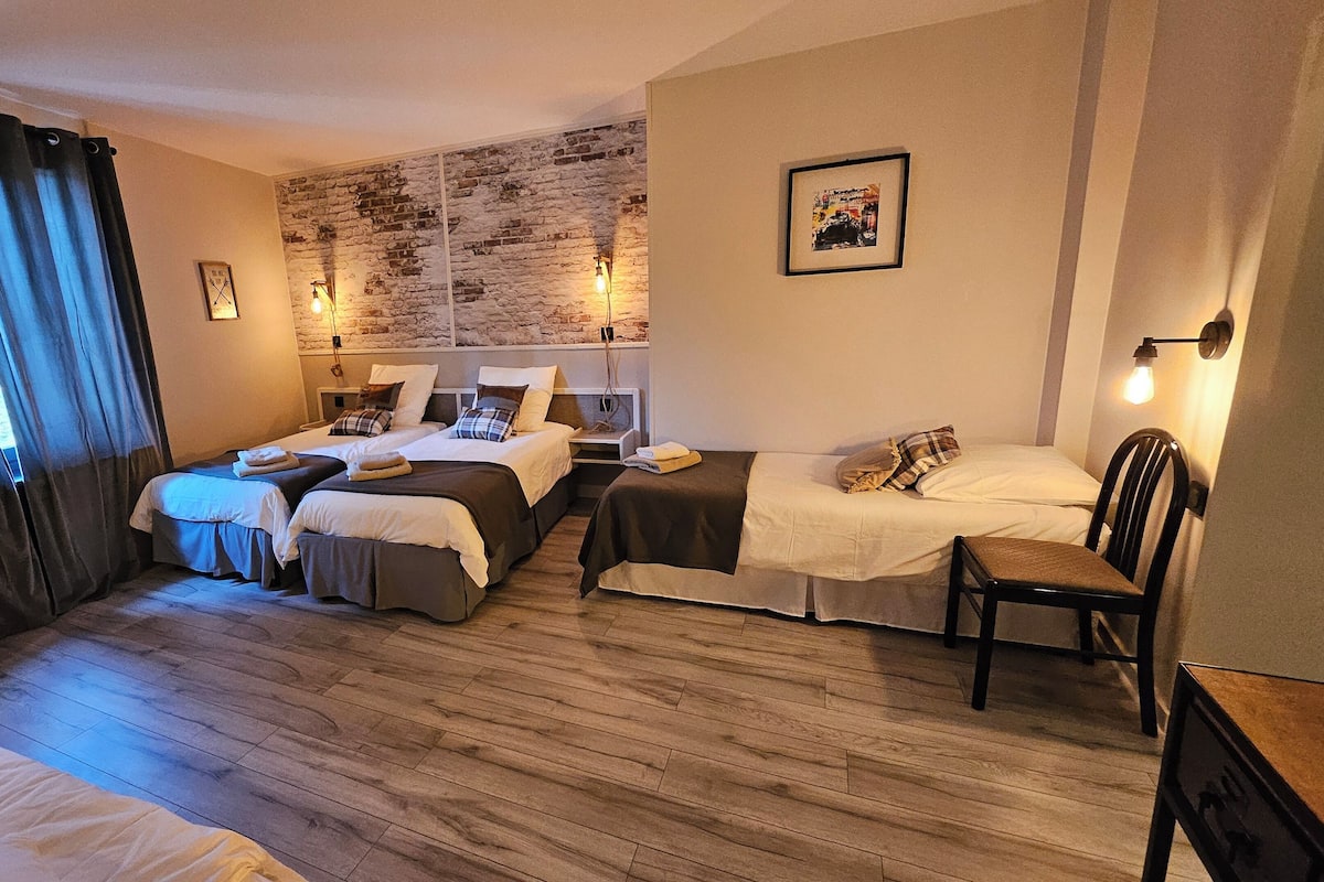 Een hotelkamer met twee enkele bedden, een kleine tafel, een stoel, een houten vloer, een bakstenen muur en een schilderij aan de muur.