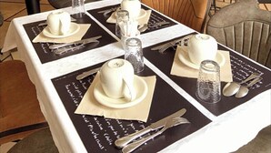 A dining area with tables set for four, each with a white tablecloth, white plates, and silverware. There are brown leather chairs and a black cabinet with shelves in the background. - AUBERGE DE LA MARINE (Losne)