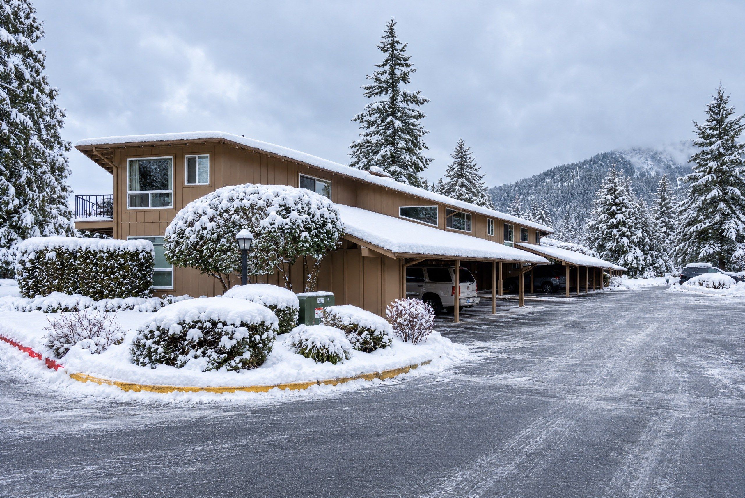 A two-story building with a covered parking area and snow-covered trees.