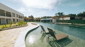 A swimming pool with lounge chairs, a pergola, and a modern building with balconies.