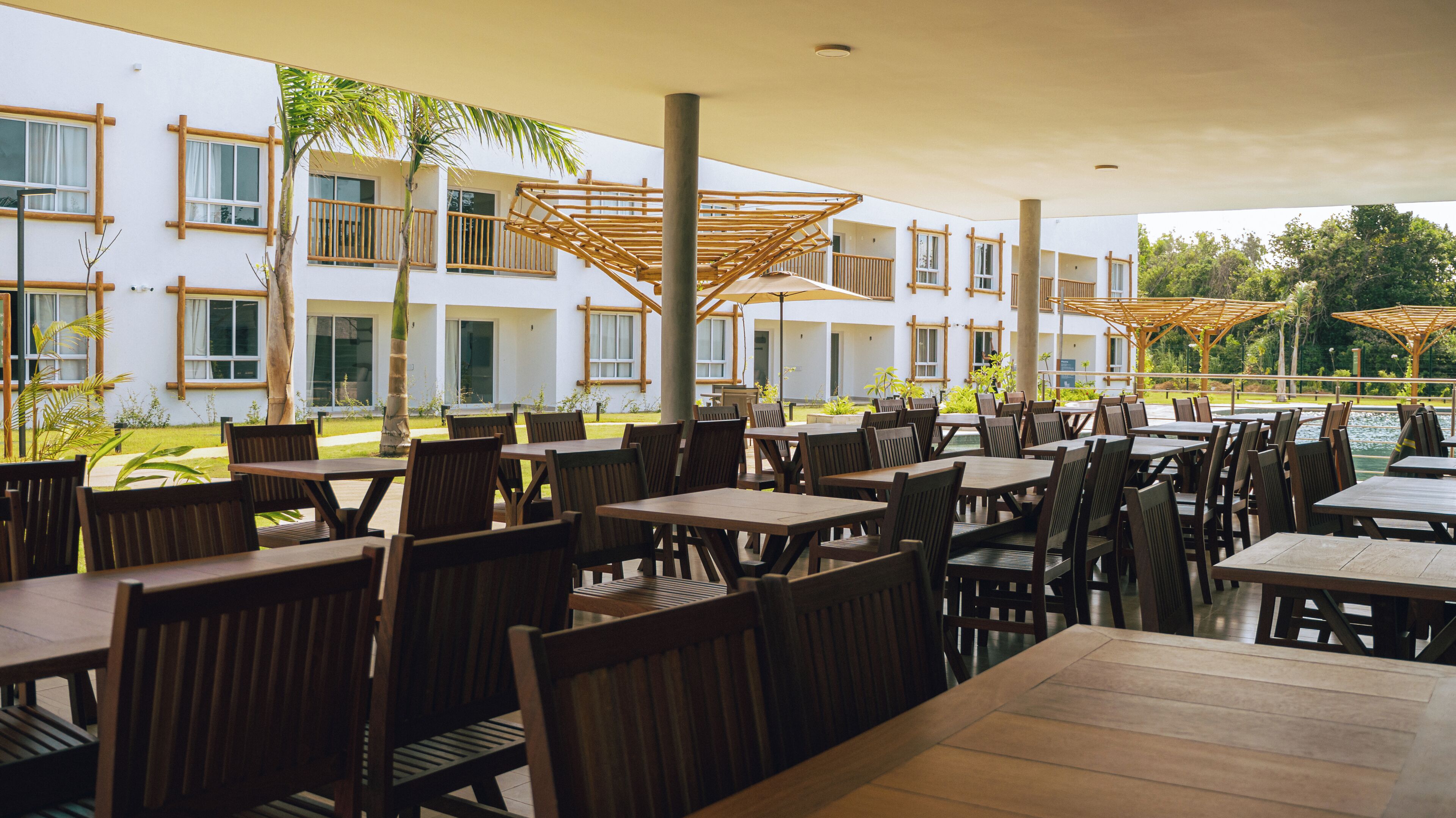 An outdoor seating area with wooden tables and chairs, surrounded by a white building with large windows and wooden balconies.