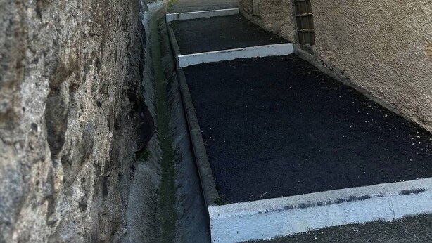 Een smalle steeg tussen gebouwen met een geplaveid pad dat leidt naar een klein binnenhof.