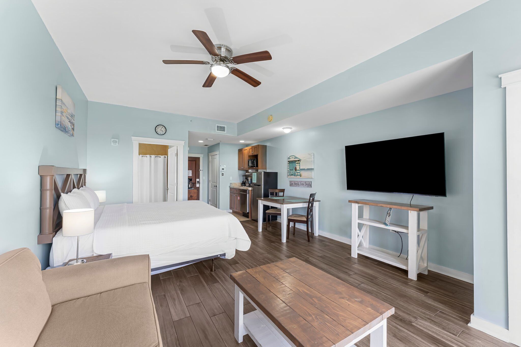 A bedroom with a bed, a desk, a chair, a TV, and a ceiling fan.