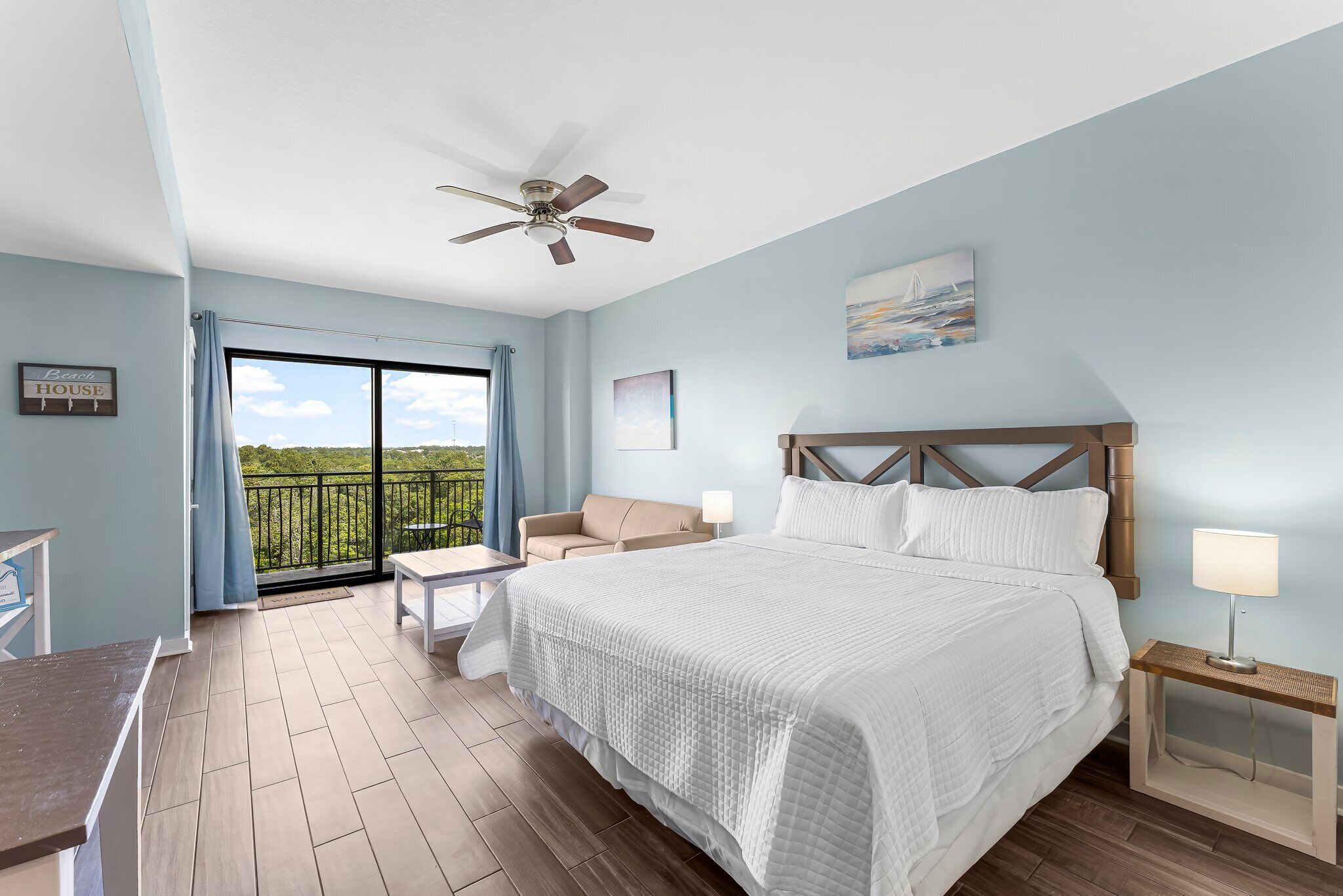 Un dormitorio con cama, ventilador de techo, mesita de noche, lámpara, silla, mesa y balcón con vistas.
